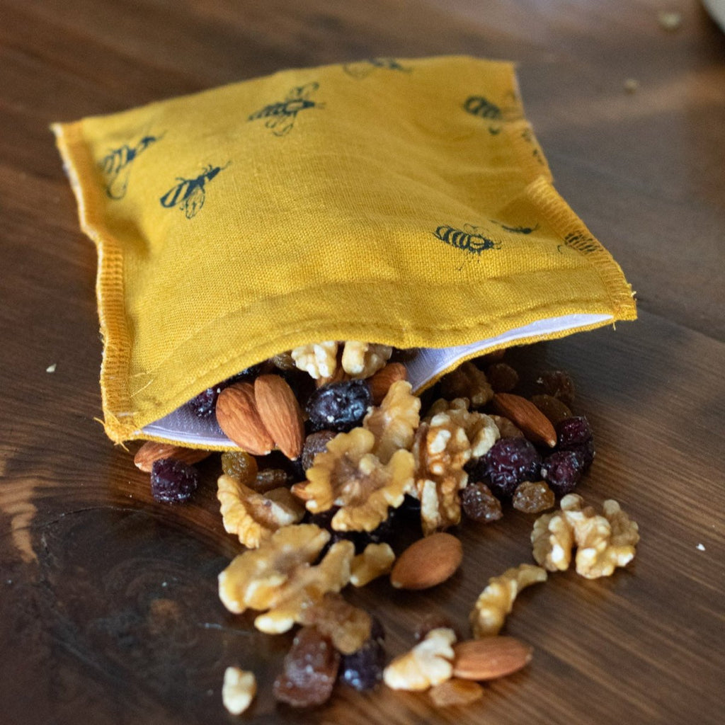 Bee Mustard Linen Snack Bag toppled over with Nuts and Raisins on countertop.  From the Honey Bee Collection by Helen Round.