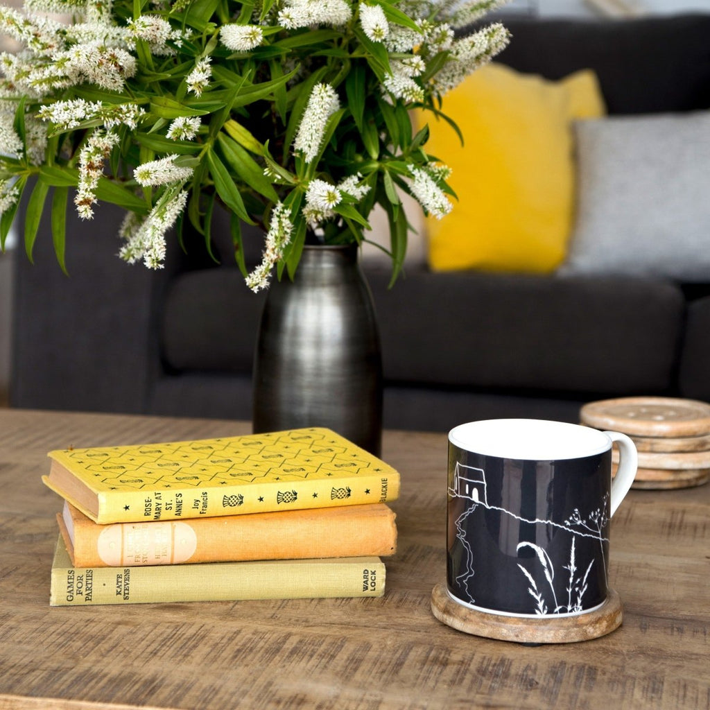 Rame Head Mug in Dark Grey bone china next to books and vase of flowers on a table from a collection by Helen Round