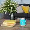 Rame Head Mug in Turquoise Blue Bone China with books and flowers in living room on a table from a collection by Helen Round