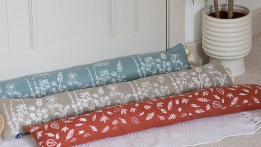Three Linen Draught Excluders in Garden and Leaf Designs placed on the floor next to a door from Helen Round
