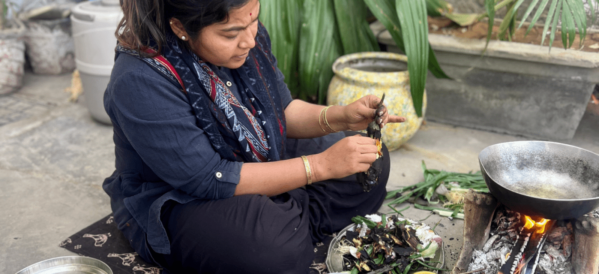 Indian lady sitting on the floor by an open fire removing the skin from smoked aubergines