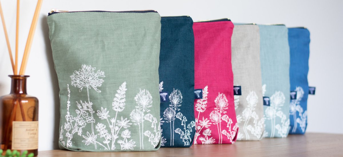 Selection of Large Linen Toiletry Bags pictured overlapping with white floral print from the Garden Collection by Helen Round