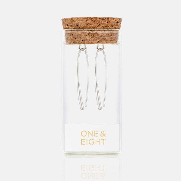 Silver earrings in class tube with cork lid in a clear box labeled 'One & Eight' on a white background
