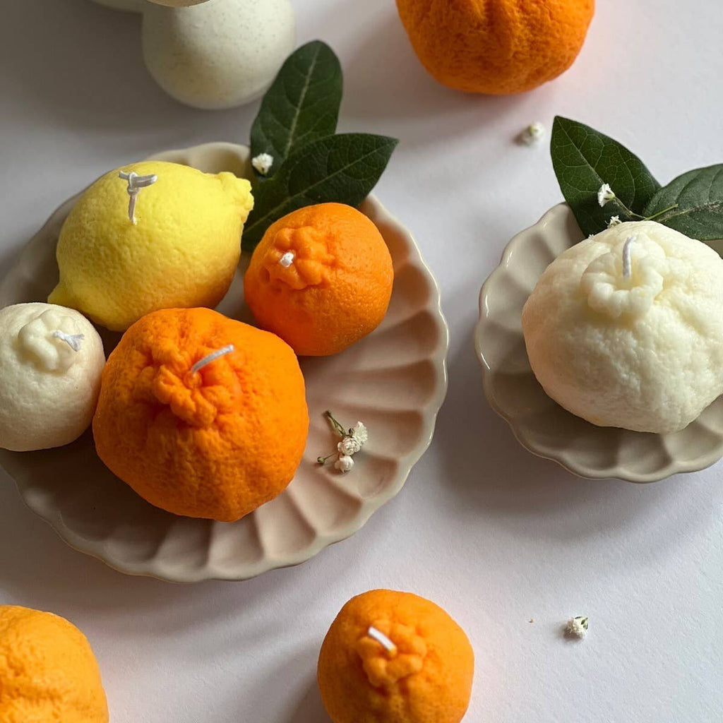 Decorative candles shaped like fruits and flowers on a white surface