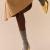 Person wearing gold shoes and grey merino socks on a beige background