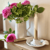 Bouquet of pink and green flowers in a vase with a candle on a wooden surface.