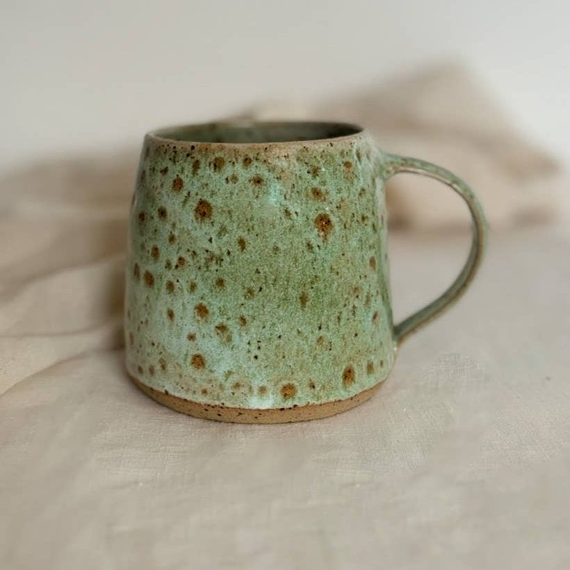 Green ceramic mug with speckled pattern on a beige surface so;ld By Helen round