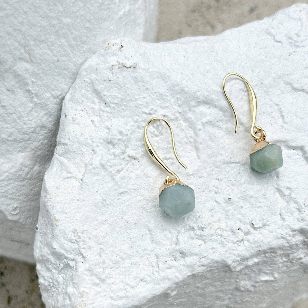 Gold earrings with green gemstones on a textured white surface sold by Helen Round