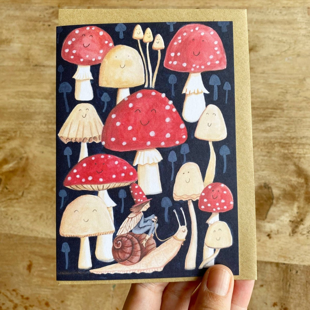 Card with cartoon mushrooms and a snail on a wooden surface