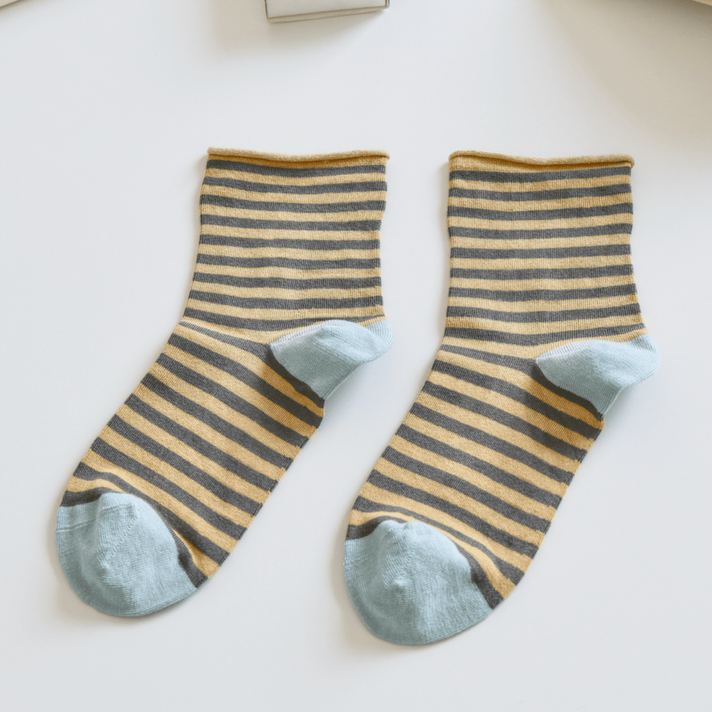 Striped socks with green toes on a light surface, next to a keyboard and book Sold by Helen Round