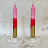 Two pink and gold candles on white candle holders against a textured beige background