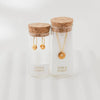 Two glass jars with cork lids containing gold jewelry on a white background