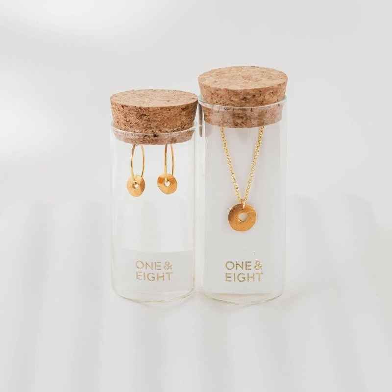 Two glass jars with cork lids containing gold jewelry on a white background