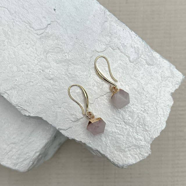 Pair of gold earrings with pink gemstones on a textured white surface sold by Helen Round