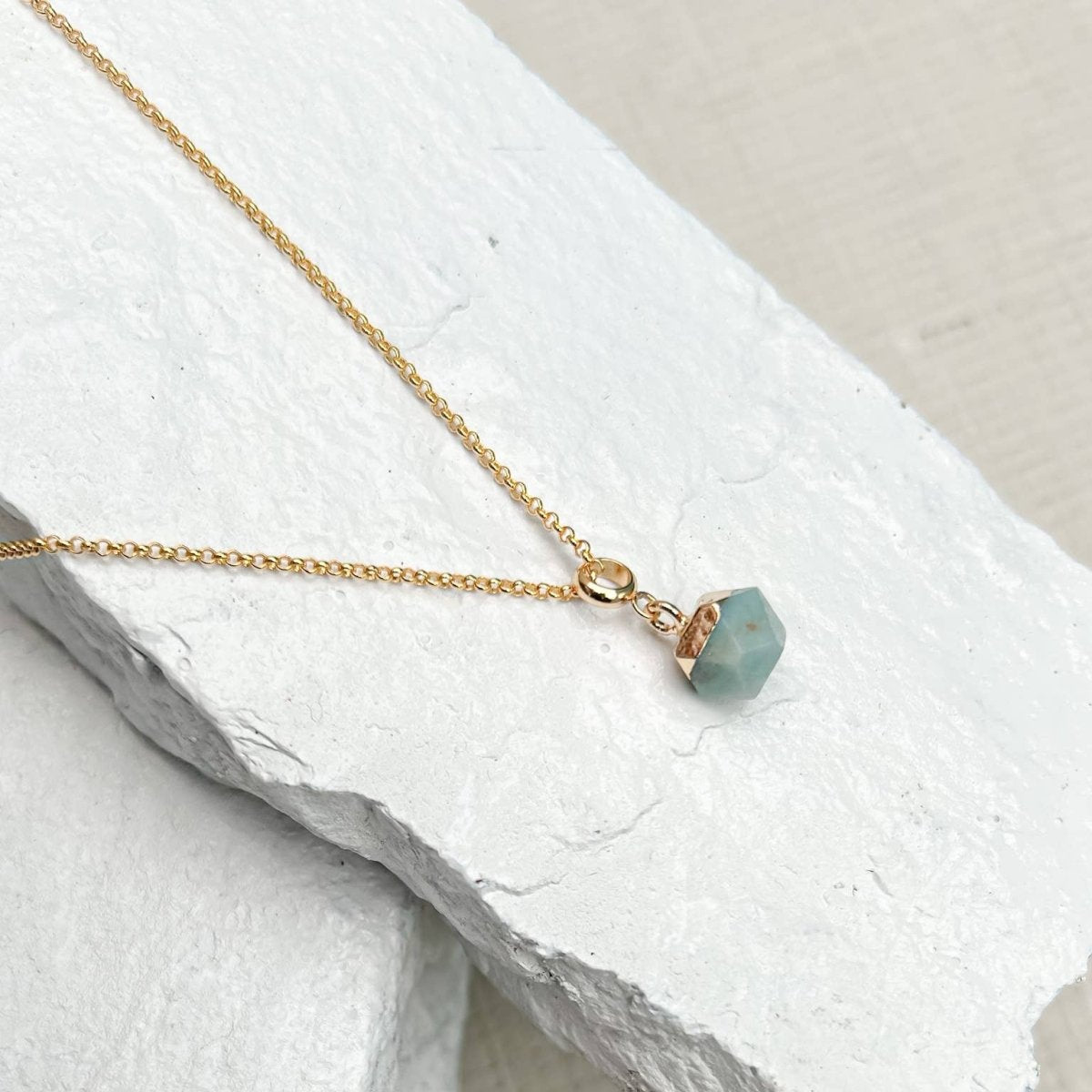 Gold necklace with a green pendant on a white stone surface ssold by Helen Round