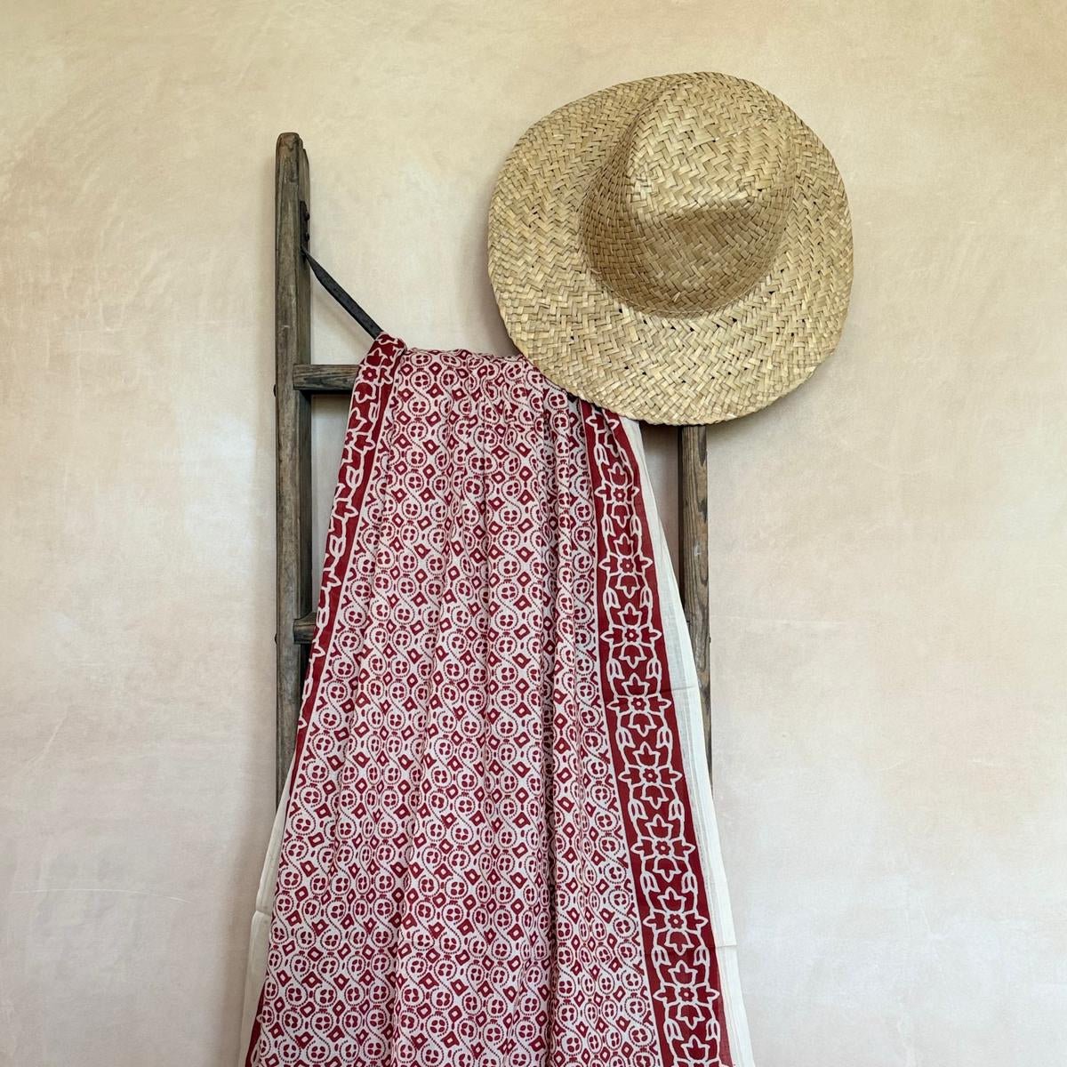 Red and white patterned sarong draped over a wooden ladder against a beige wall.