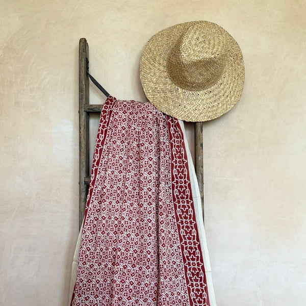 Red and white patterned sarong draped over a wooden ladder against a beige wall.