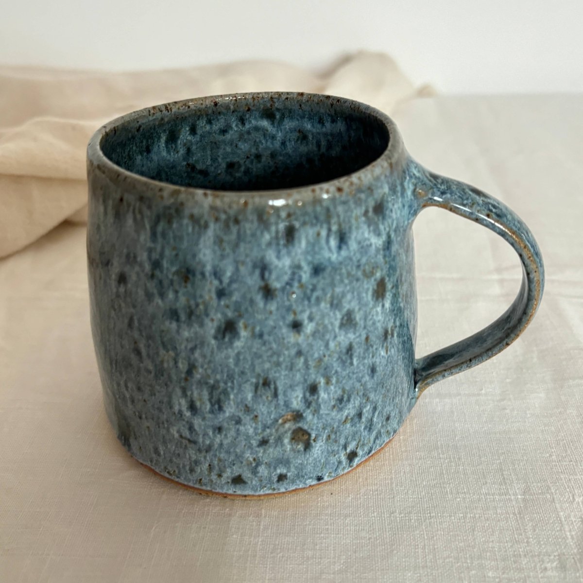 Blue ceramic mug with speckled texture on a beige surface, sold by Helen Round