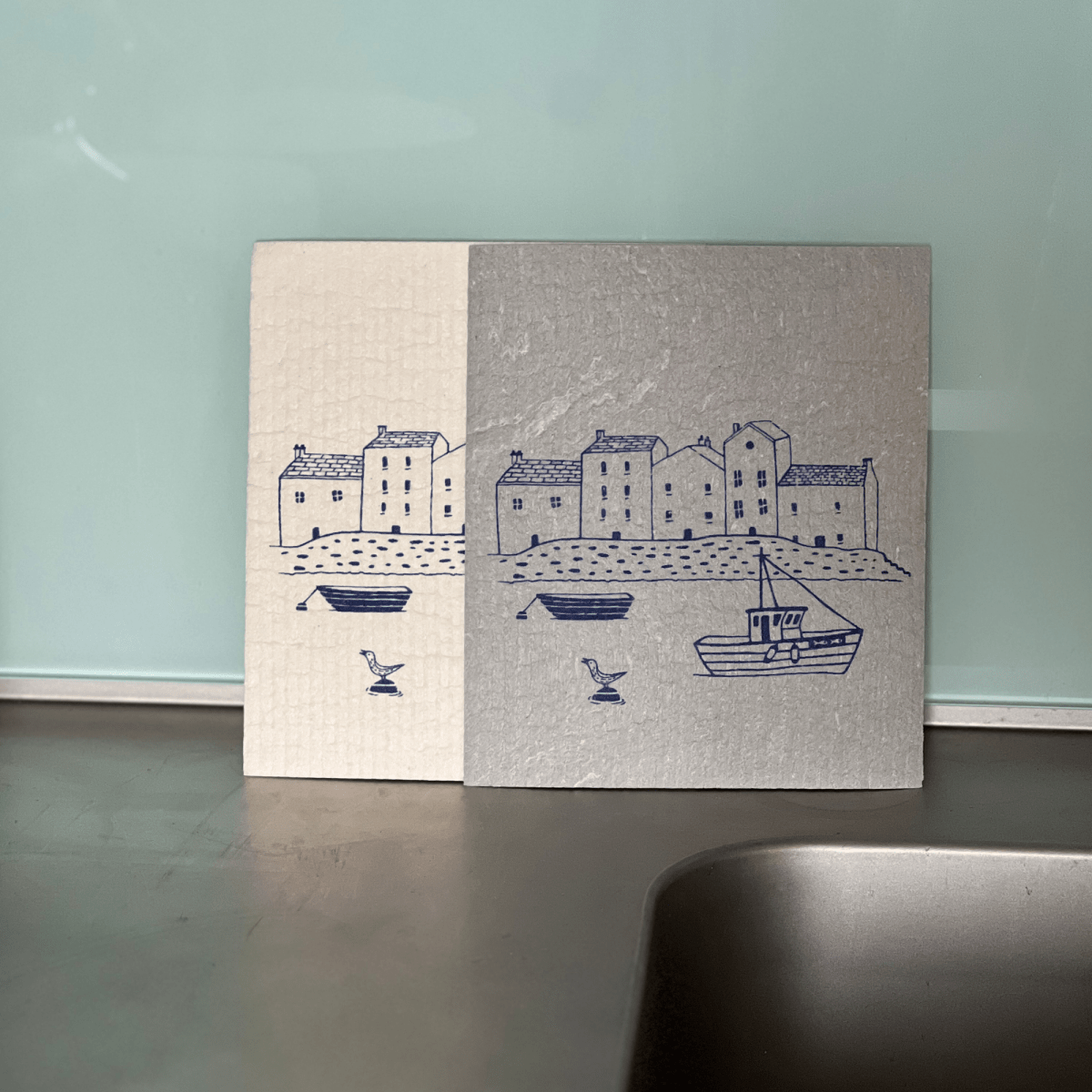 Two fabric panels with coastal illustrations on a kitchen counter.