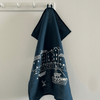 Navy blue linen tea towel with white graphic design hanging on a white rack against a beige wall from a collection by Helen Round.