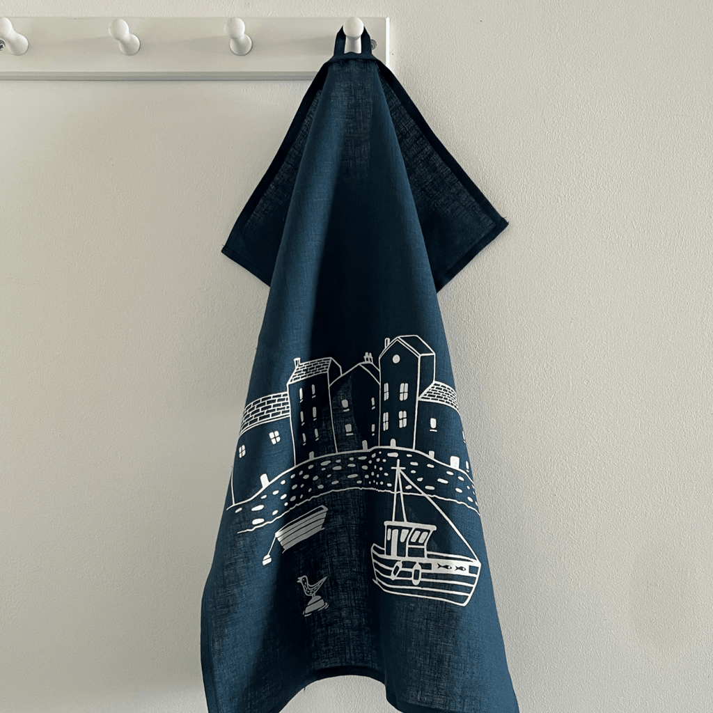 Navy blue linen tea towel with white graphic design hanging on a white rack against a beige wall from a collection by Helen Round.
