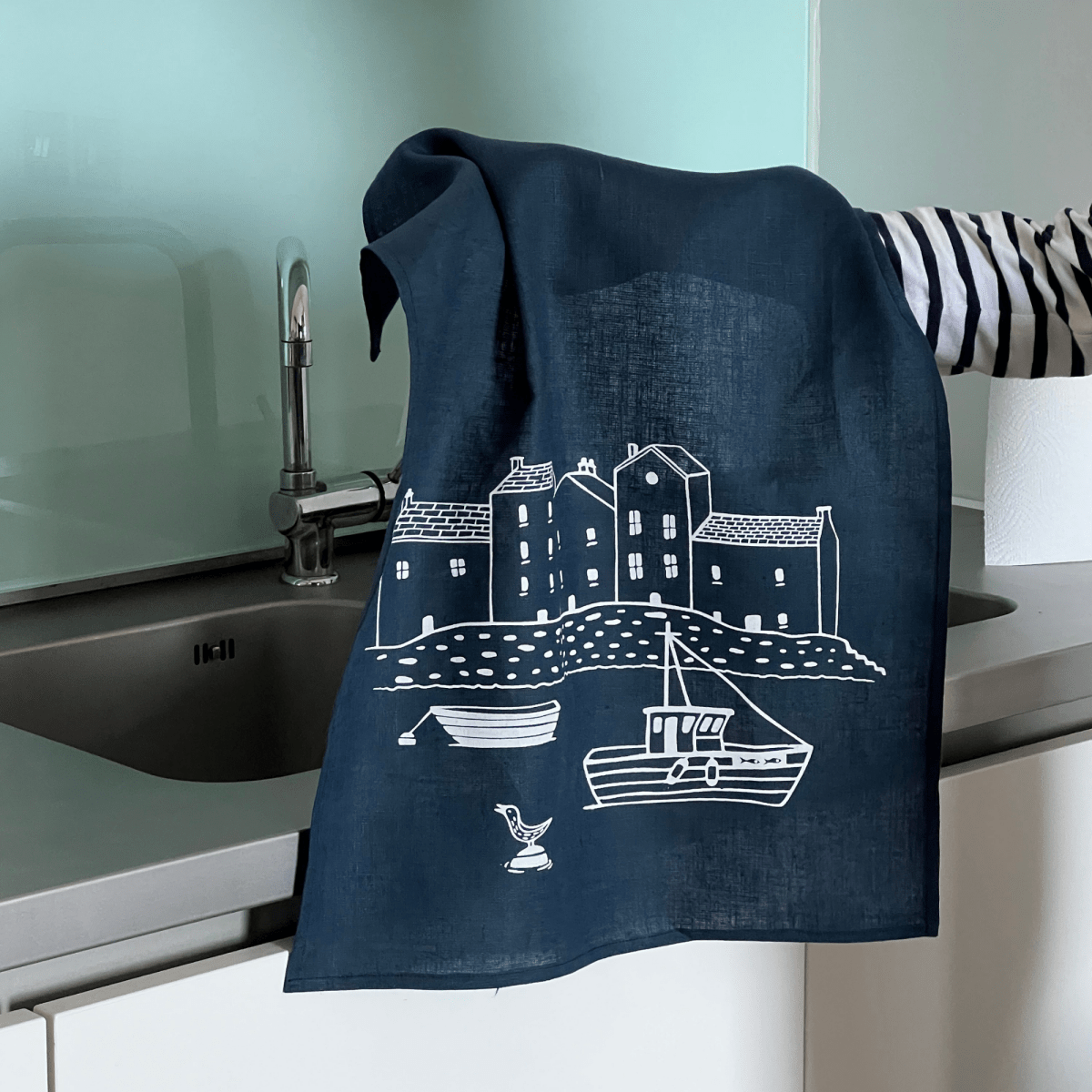 Navy blue linenn tea towel with white coastal design hanging over a kitchen sink.