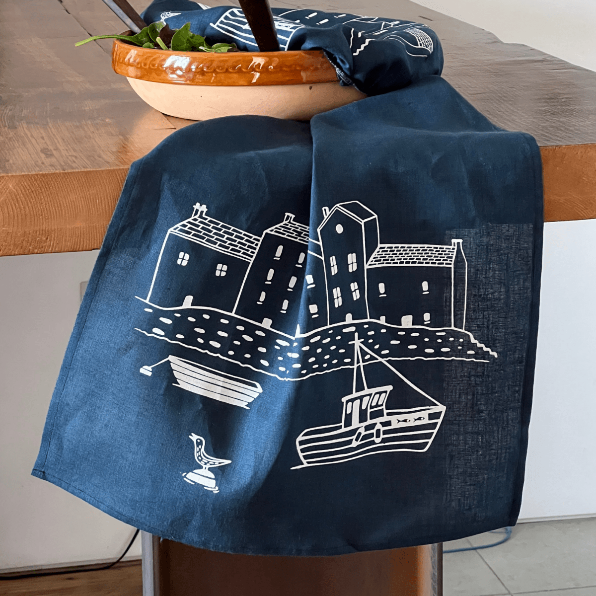 Navy blue linen tea towel with white house and boat design draped over a chair from Helen Round.