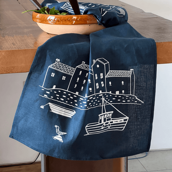 Navy blue linen tea towel with white house and boat design draped over a chair from Helen Round.