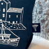 Navy blue linen fabric with white screen printed design of a house and boat, with a brand label in the corner from Helen Round.
