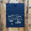 Navy blue tea towel with white printed design of a coastal scene on a wooden surface by Helen Round 