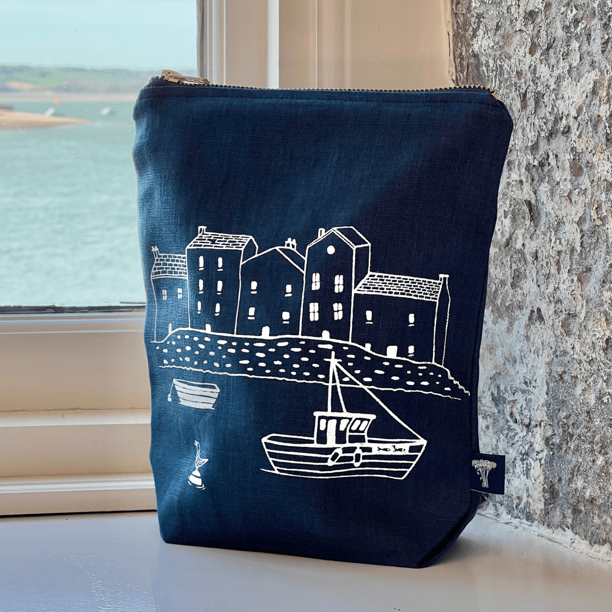 Navy linen pouch with white illustration of a coastal scene on a windowsill.
