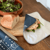 Sandwich with lettuce on a wooden board with bread and a knife, wrapped in a blue reusable linen sandwich wrap from Helen Round.