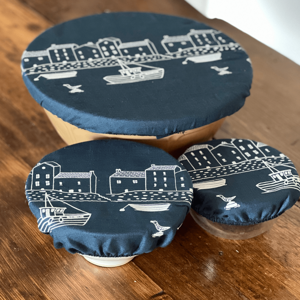 Set of three blue linen bowl covers with white designs on a wooden surface from Helen Round.