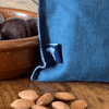 Blue linen snack bag with a white logo on a wooden surface next to almonds and a terracotta bowl from Helen Round.