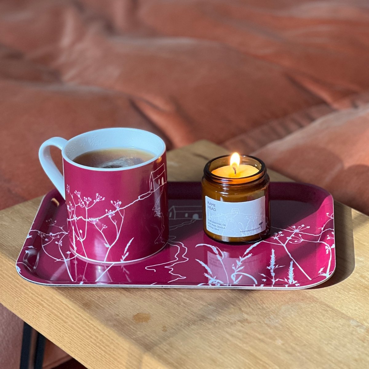 Helen Round bone china mug, Rame Head candle and Rame Head Tray all with an illustrations of Rame Head in white on a raspberry background.