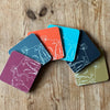 Six colourful coasters featuring the Rame Head design from Helen Round fanned out of a wooden surface.