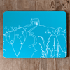Tuquoise blue placemat with white Rame Head design on a wooden surface from Helen Round.