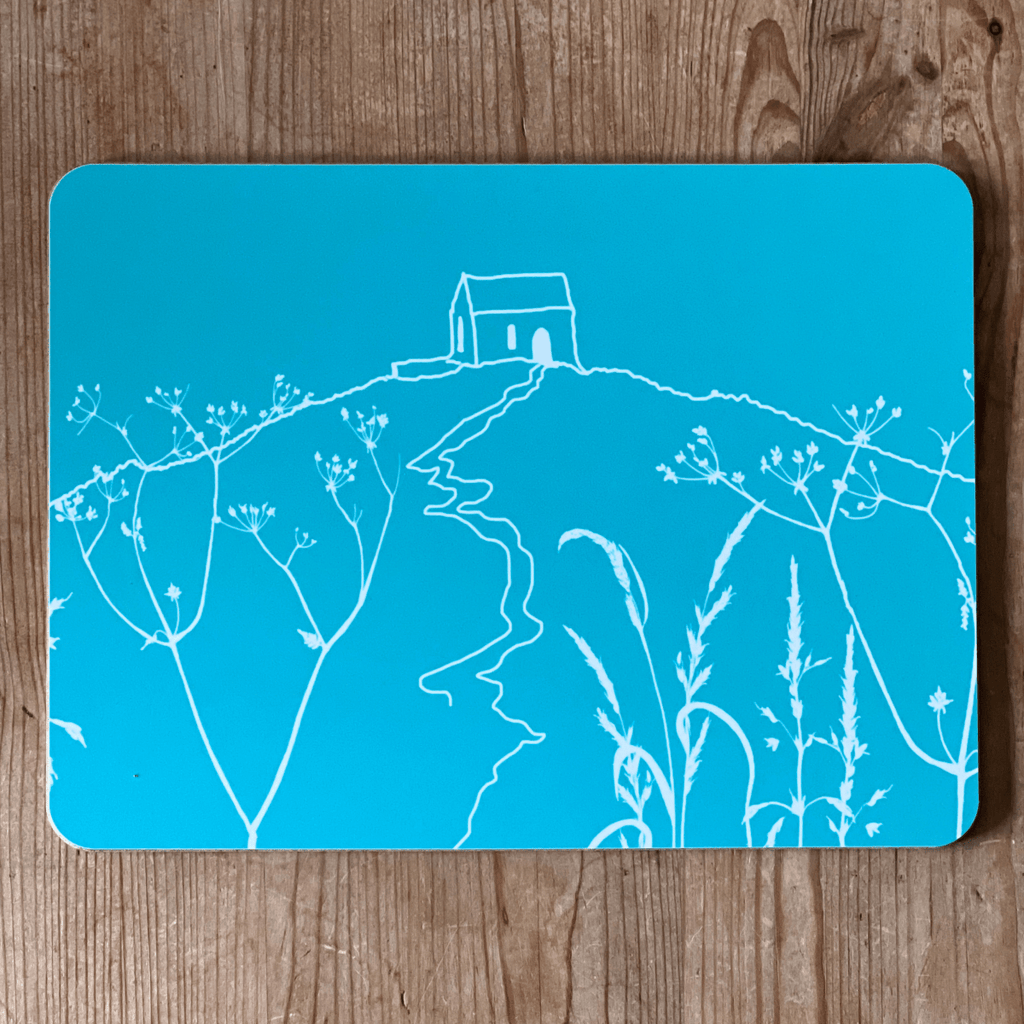 Tuquoise blue placemat with white Rame Head design on a wooden surface from Helen Round.