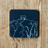 Dark Navy/black coaster with white Rame Head design placed on a wooden surface from Helen Round.