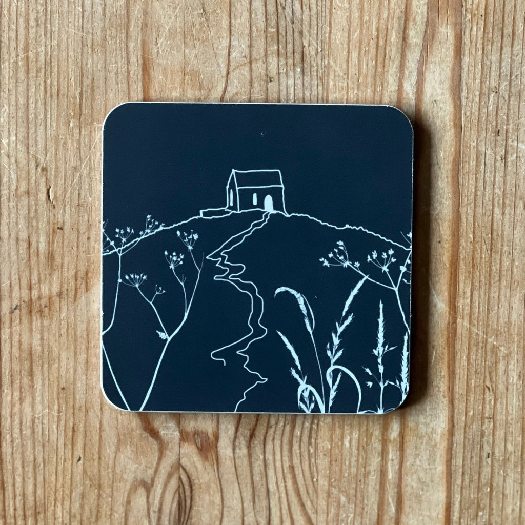 Dark Navy/black coaster with white Rame Head design placed on a wooden surface from Helen Round.