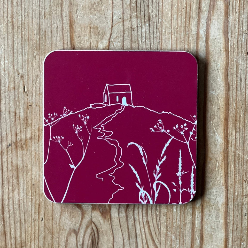 Raspberry red coaster with white Rame Head design placed on a wooden surface from Helen Round.