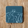 Slate grey coaster with a white Rame Head design, placed on a wooden surface from Helen Round.