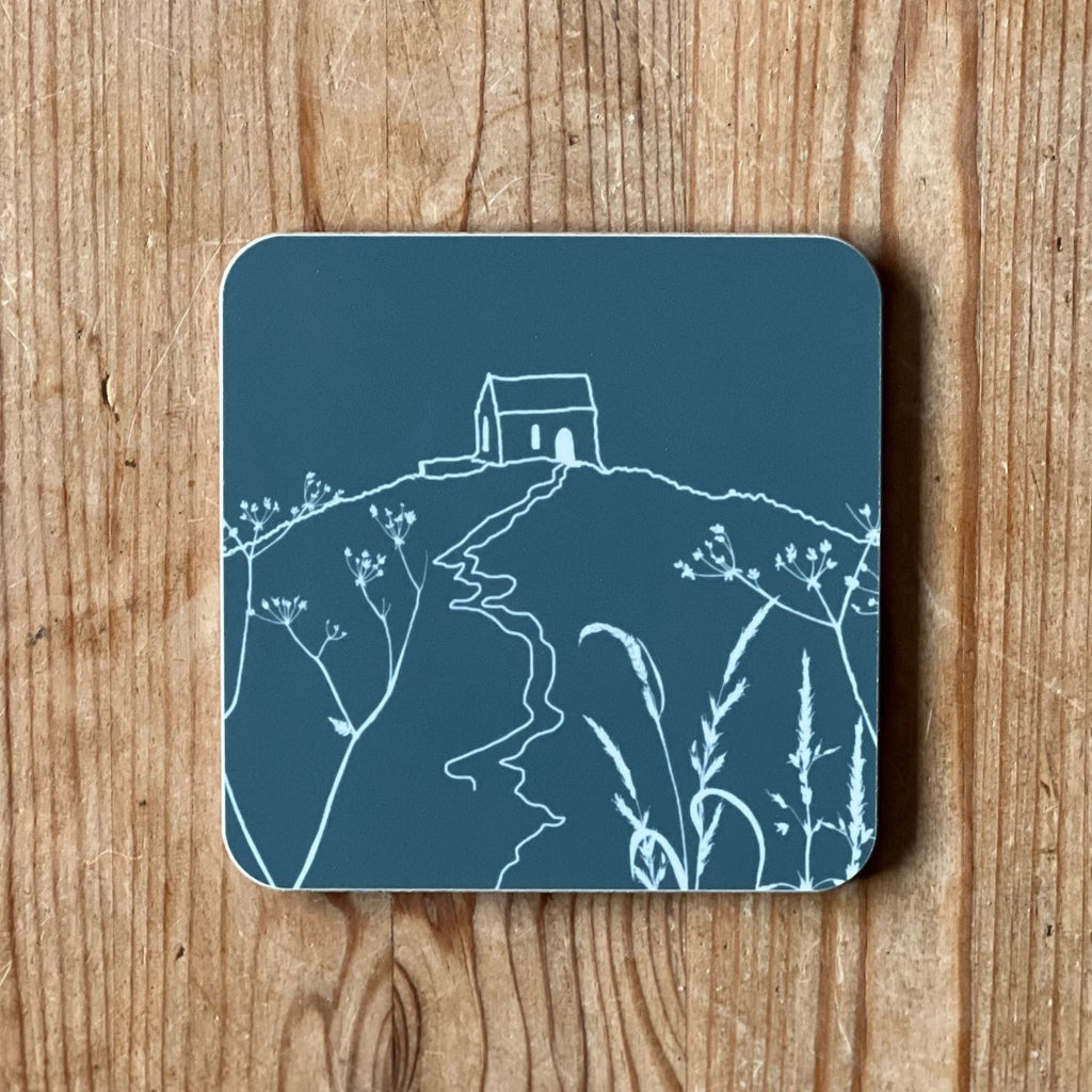 Slate grey coaster with a white Rame Head design, placed on a wooden surface from Helen Round.