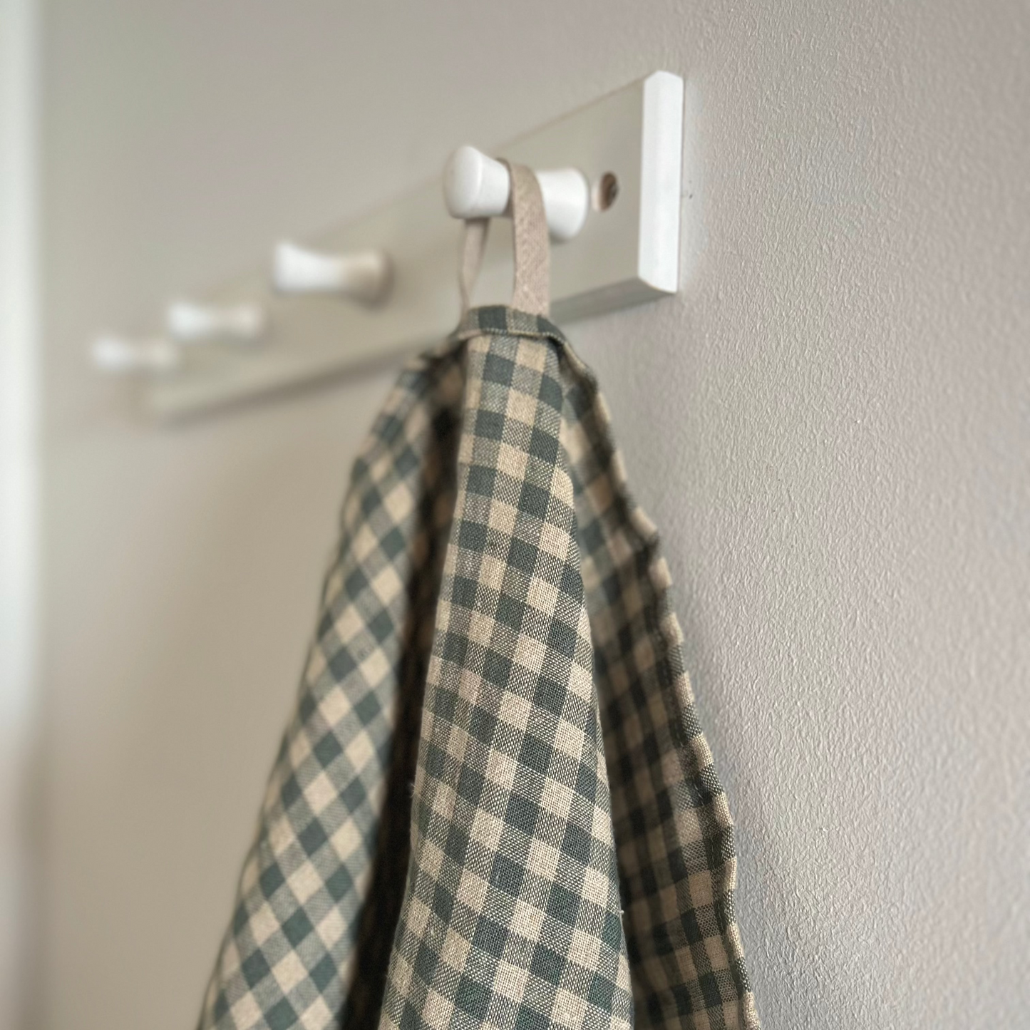 Sea Green Check Linen Tea Towel hung on a white wooden peg by a linen hook from the Check Collection by Helen Round