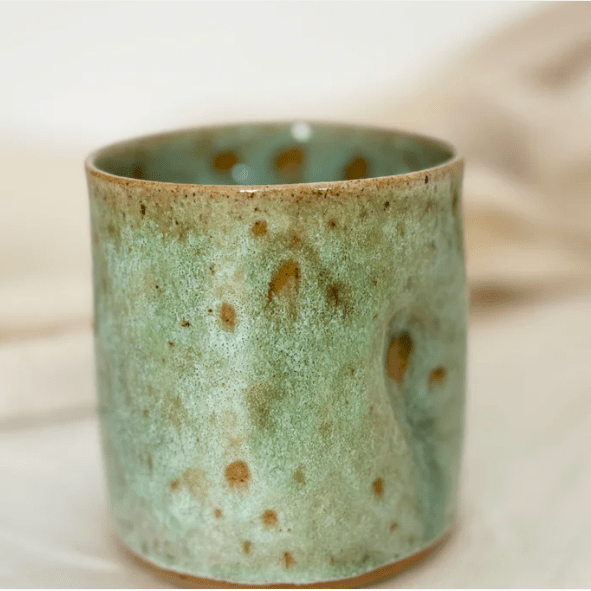 Green ceramic cup with brown speckles on a light background