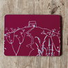 Placemat with white Rame Head design on a raspberry red background placed on a wooden surface from Helen Round