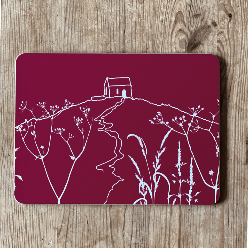 Placemat with white Rame Head design on a raspberry red background placed on a wooden surface from Helen Round