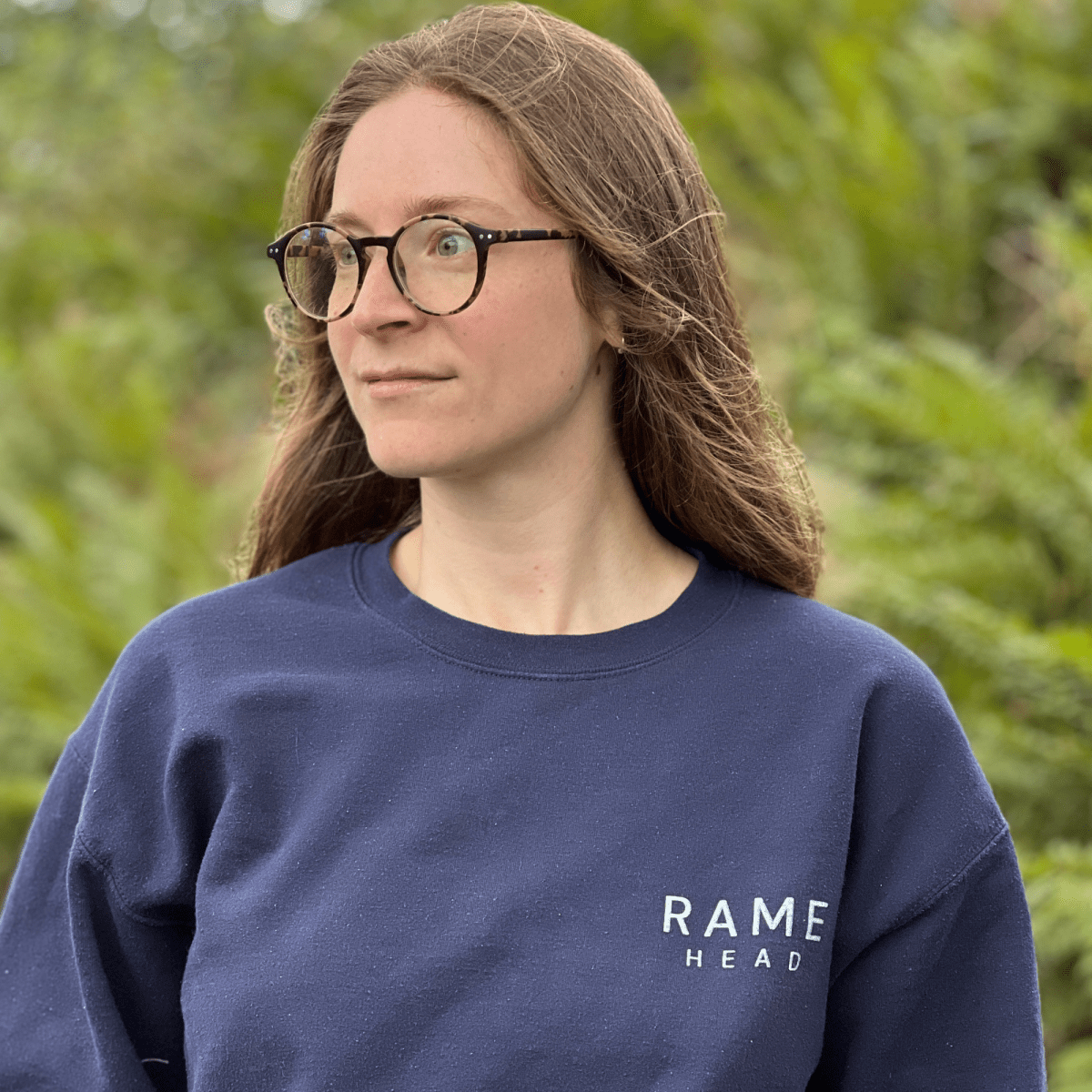 A navy blue crewneck sweatshirt with 'RAME HEAD' printed in white on the chest, with an illustration of Rame Head on the back from Helen Round