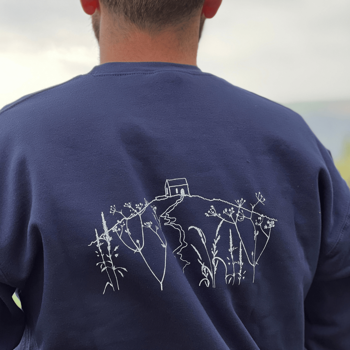 A  Navy Blue  crewneck sweatshirt with 'RAME HEAD' printed in white on the chest With an illustration of Rame Head on the back from Helen Round