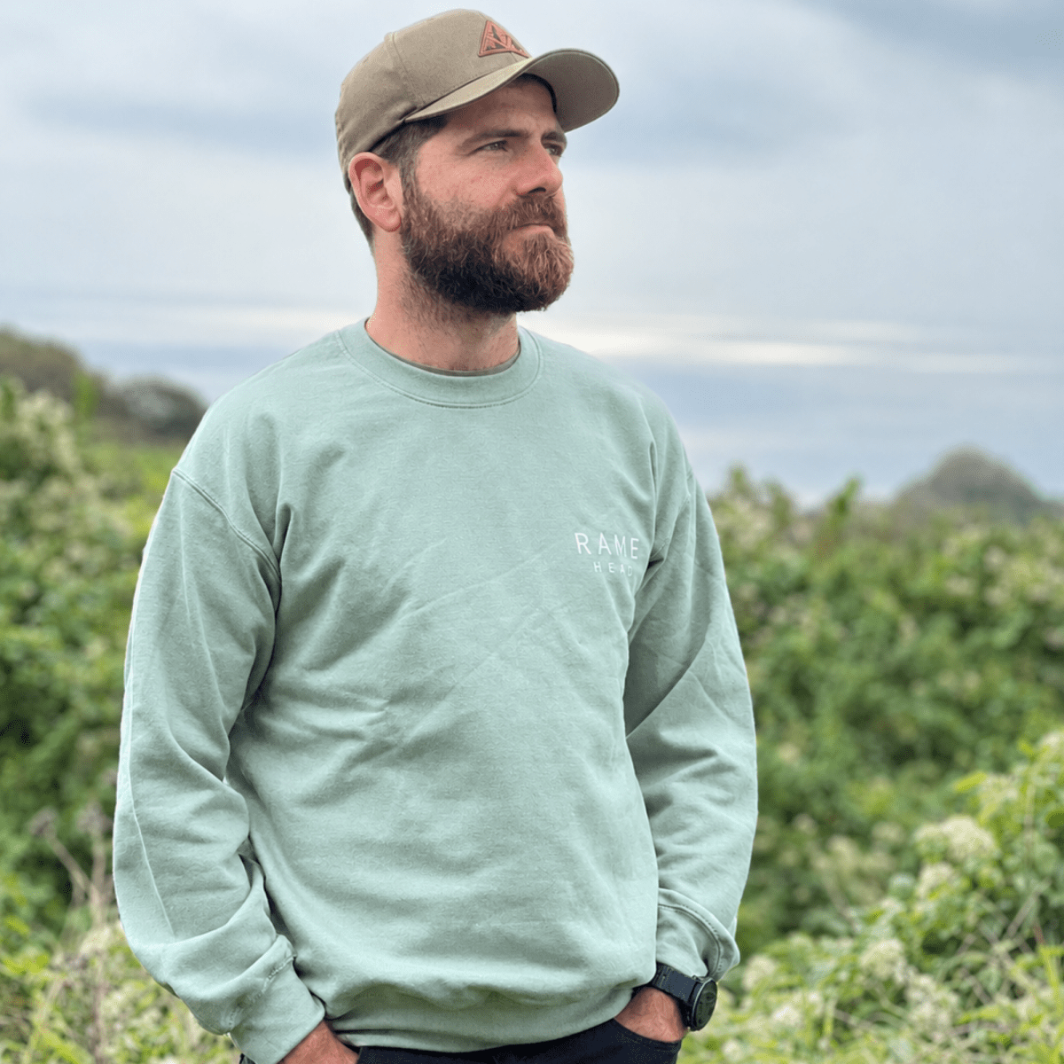 A sage green crewneck sweatshirt with a small white hand-screen-printed Rame Head logo on the chest. 